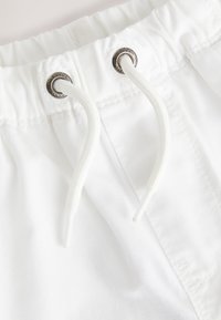 White fabric featuring a drawstring waist. Metal grommets with a smooth finish. The texture appears soft and lightweight.