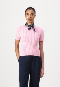 Pull en tricot rose clair à manches courtes avec un motif en relief et une bordure côtelée, associé à un pantalon bleu marine et une écharpe à motifs bleus.
