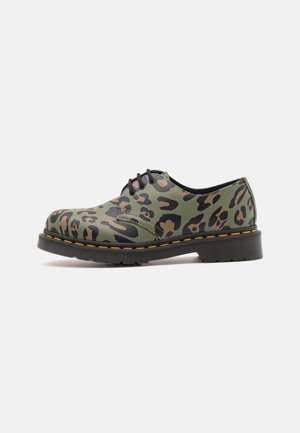 Chaussure à lacets à talon bas avec motif léopard vert et marron, semelle noire et détail de couture jaune, présentée de profil sur fond blanc.
