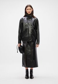 Crna kožna jakna s visokim ovratnikom, uparena s odgovarajućom crnom kožnom suknjom s kontrastnim šavovima. Dodatak: mala crna torba.