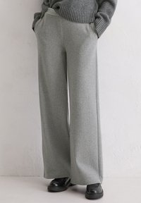 Pantalon gris à jambes larges avec un motif à fines rayures verticales, confectionné dans un tissu texturé. Comprend des poches latérales et une coupe ample.