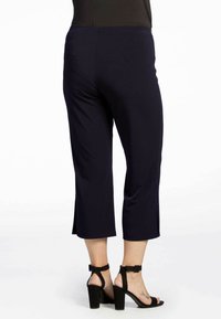 Navy capri-broekjes van soepel materiaal, met een middelhoge taille en een zijsplit aan de zoom, gecombineerd met zwarte hoge hakken.