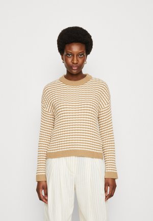 Maglione a righe beige e crema con scollo rotondo a costine e polsini, realizzato in materiale a maglia testurizzato, indossato con pantaloni a righe.