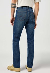 Jeans de mezclilla azul con un diseño de pierna recta, costuras visibles y dos bolsillos traseros que presentan un patrón ondulado distintivo.