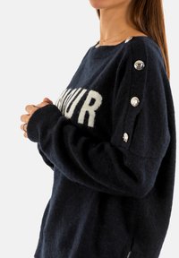 Maglione in lana navale con vestibilità oversize, caratterizzato da testo bianco "AMOUR" e dettagli con bottoni argentati sulle spalle. Morbido al tatto con polsini a costine.