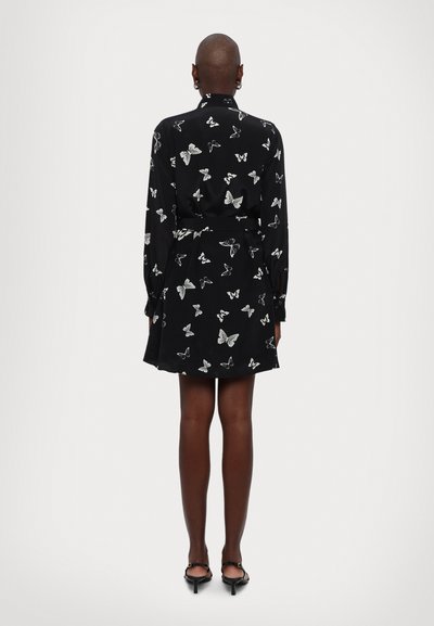 Abito nero con motivi a farfalla bianchi, maniche lunghe, vita con cintura e fondo svasato. Tessuto liscio con un design del colletto classico.