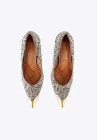 Scarpe con tacco a punta ricoperte di scintillanti strass argentati con un'accento metallico dorato sulla punta. Fodera interna in tessuto trapuntato marrone.