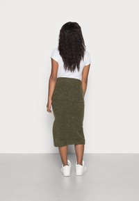 Olivgrön, stickad knälång kjol med en figurnära design, kombinerad med en vit kortärmad topp och vita sneakers. Slät textur.