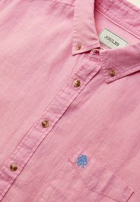Chemise rose pour homme avec col boutonné, boutons beige et petit logo bleu brodé sur la poche poitrine.