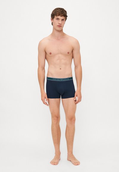 Boxers pour homme de couleur marine avec une texture douce, ceinture élastique arborant le logo "Emporio Armani" en vert foncé, design ajusté et longueur de jambe courte.