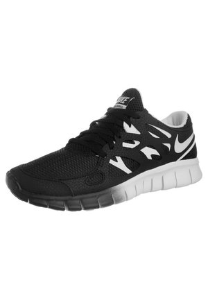 Chaussure de course Nike noire et blanche avec empeigne en mesh, fermeture à lacets et semelle flexible rainurée, inclinée pour montrer le côté extérieur.