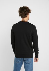 Sudadera negra con cuello redondo y puños acanalados. Material de algodón suave, que presenta un corte clásico y relajado con un diseño liso.