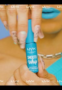 NYX Smooth Whip Matte Lip Cream i en cylindrisk turkos tube med vit text hålls mellan fingrarna med ljusrosa, mönstrade naglar.