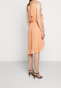 Robe pêche au design asymétrique, une épaule avec volants, taille cintrée et ourlet évasé. Complétée par des talons hauts noirs à lanières.