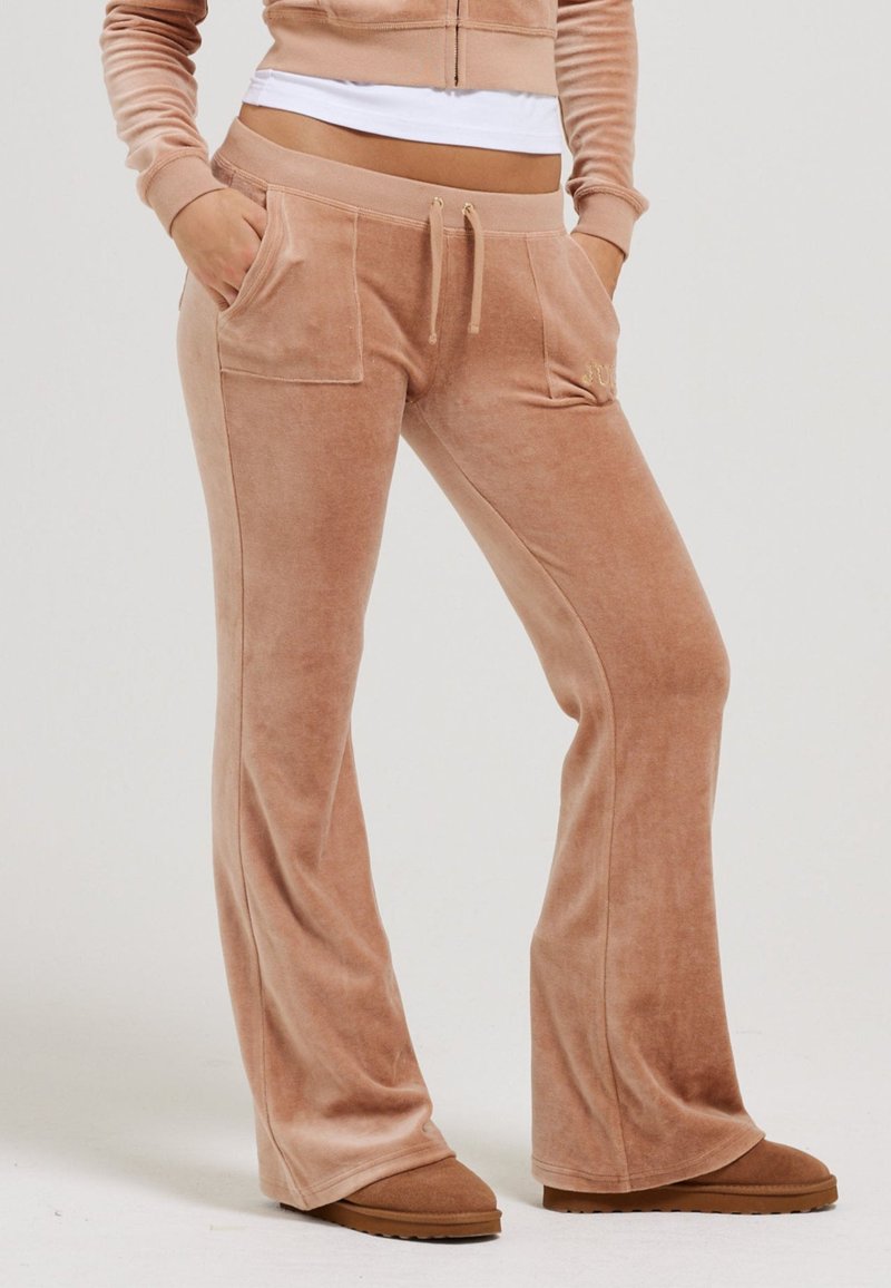 Ecru gekleurde flared velours broek met voorzakken, een elastische tailleband en decoratieve trekkoord. Zachte textuur en ontspannen pasvorm.