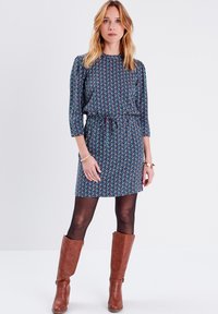 Vestido con estampado floral en azul oscuro, con mangas 3/4, cintura ceñida y corte holgado, combinado con botas marrones hasta la rodilla.