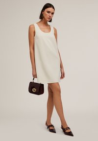 Rochie crem fără mâneci, siluetă în formă de A, textură netedă. Geantă de mână bordeaux închis cu accesorii aurii și pantofi cu vârf ascuțit și curele.