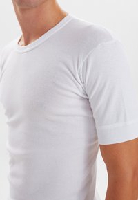 Hvid kortærmet t-shirt lavet af letvægts bomuld. Har en ribbet rund halsudskæring og en glat tekstur med en tætsiddende silhuet.