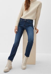 Blå högmidjade jeans med smal passform, i kombination med en krämfärgad stickad tröja. Outfiten kompletteras av beige snörstövlar.