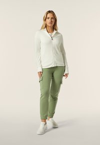 Felpa bianca con zip e maniche lunghe, abbinata a pantaloni cargo verde oliva. Sneakers bianche completano l'outfit. Tessuti con texture lisce.