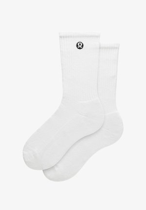 Par hvide ankelsokker med ribbet kant og et lille sort cirkulært logo nær toppen.