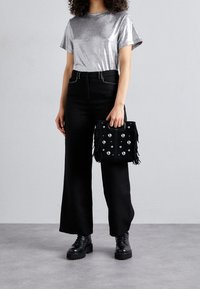 Silvrig metallisk kortärmad t-shirt, hög midja svarta vida byxor, svart franshandväska med metallnitar och svarta chunky boots.