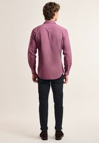 Camisa de manga larga de tela rosa claro, con cuello abotonado y dobladillo recto, combinada con jeans oscuros y zapatos marrones.