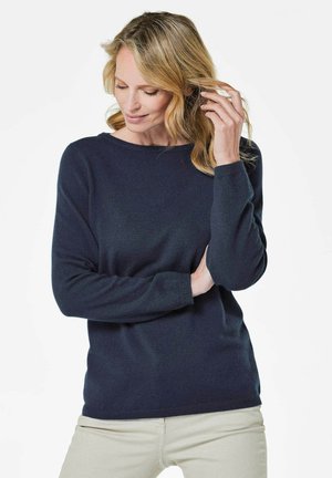 Pull en laine bleu marine à manches longues et col rond, avec une texture douce et une coupe décontractée, associé à un pantalon beige clair.