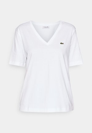 Biała koszulka V-neck wykonana z bawełny, z krótkim rękawem, z małym zielonym logo krokodyla na lewej piersi. Prosty design i lekka konstrukcja.