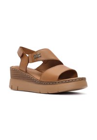 Sandalias de cuña de cuero marrón con un diseño de tiras cruzadas, punta abierta y suela texturizada. Presentan herrajes de marca y costuras en contraste.