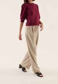 Bordeaux kortærmet sweater med puffede skuldre, parret med beige bredbenede bukser og sorte hæle-sandaler med en knyttet design.