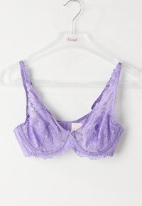 Lilla blond underwire-bh med delikate blomster mønstre hengende på en klar plastkleshenger mot hvit bakgrunn.