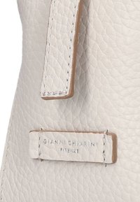 Witte textuur leren tas met een gladde beige schouderband en een metalen logo tag met de tekst "GIANNI CHIARINI FIRENZE." Schone, minimalistische ontwerpen.