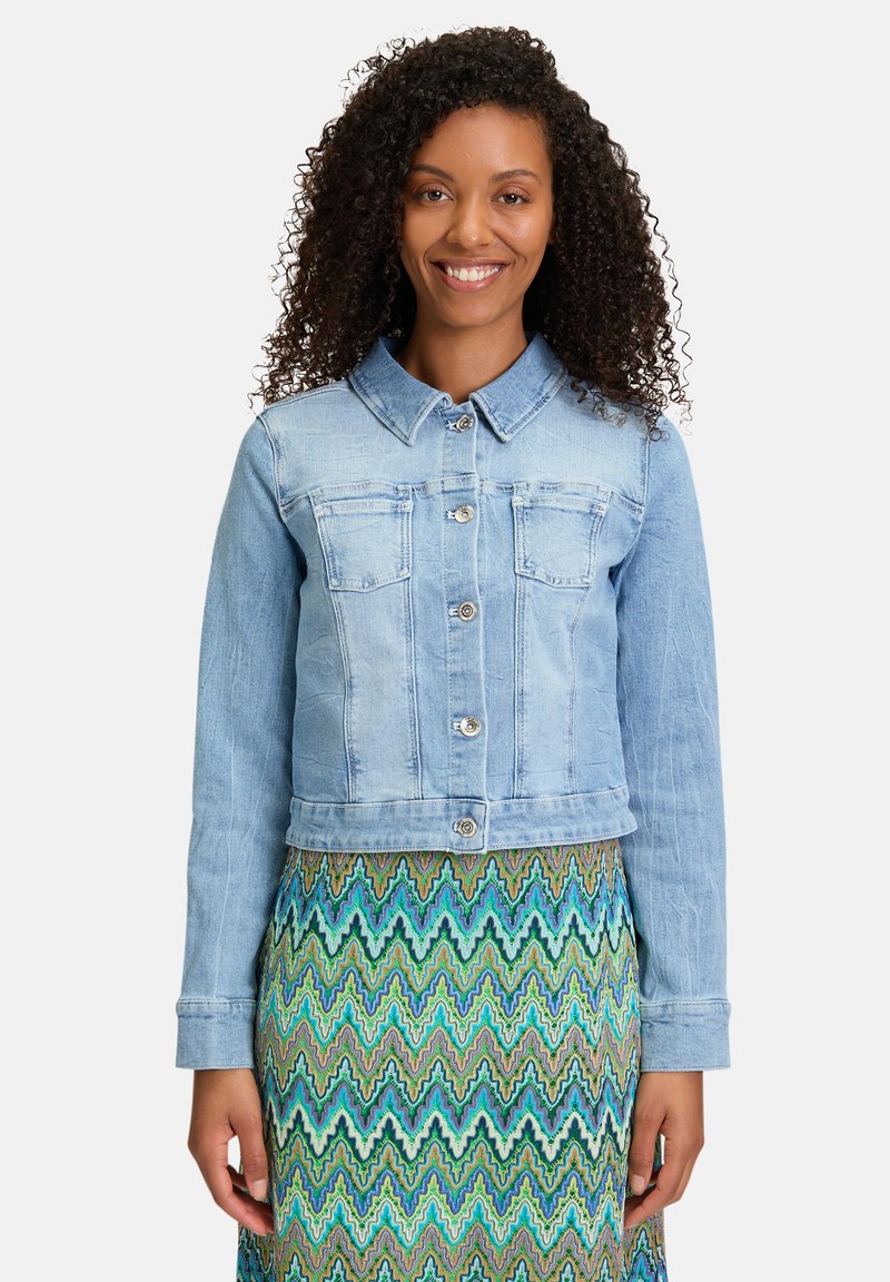 Veste en denim bleu clair avec col, fermeture à boutons et deux poches avant. Dispose de manches longues et d'un design court.