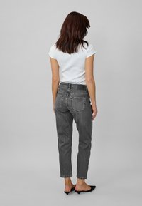 Black denim jeans with a high waist and straight cut, featuring back pockets and minimal detailing, paired with a white fitted t-shirt.