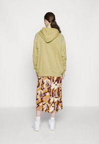 Olive green hoodie with a drawstring hood, paired with a patterned brown, orange, and lavender skirt. White sneakers complete the outfit.