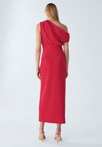 Red, one-shoulder dress with a draped top, fitted waist, and a long skirt. Smooth texture and mid-length, paired with light-colored heels.
