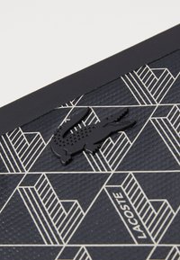 Un matériau texturé bleu marine arborant un motif géométrique en crème, avec un logo de crocodile noir affiché en évidence.