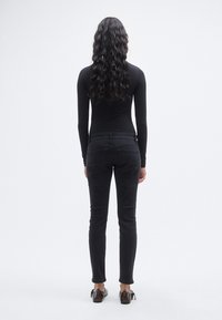  Μακρυμάνικο μαύρο τοπ και μαύρο τζιν στενής εφαρμογής με πίσω τσέπες, με ομαλή υφή και casual σχεδιασμό· φορεμένα με καφέ παπούτσια.