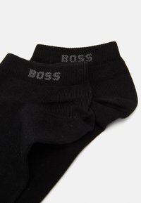 Calzini neri alla caviglia realizzati in un tessuto testurizzato, con il logo "BOSS" in grigio sulla cimossa. Il design è semplice e minimalista.