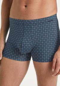 Herenslipjes van een zachte, rekbare stof. Marineblauwe achtergrond met een geometrisch ruitenpatroon in lichtblauw. Elastische tailleband.