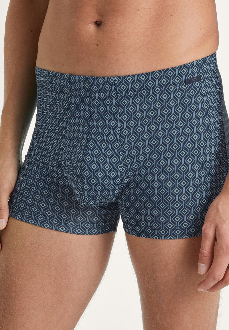 Herenslipjes van een zachte, rekbare stof. Marineblauwe achtergrond met een geometrisch ruitenpatroon in lichtblauw. Elastische tailleband.