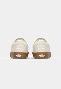 Beige semsket sko med kremfargede detaljer, bakfra. Gummisåle i lys brun, hvit "66/99" tekst, og "VANS OFF THE WALL" logo på hælen.