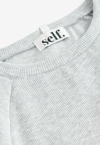 Grå ribbet sweatshirt med rund hals, der har et mærke, der læser "self." i sort på hvid baggrund. Blød tekstur med subtile striber.