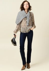 Blusa a fantasia floreale con maniche lunghe, abbinata a jeans a zampa d'elefante blu scuro. Maglione grigio appoggiato sulle spalle e stivali con tacco marroni.