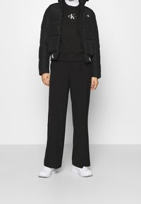 Svart vadderad jacka med en kort design, i kombination med en svart sweatshirt och vida byxor. Vita sneakers fulländar looken.