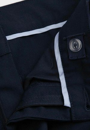 Zbliżenie na ciemnogranatowe spodnie, pokazujące pas z guzikami, zamkiem błyskawicznym i białą wewnętrzną podszewką.