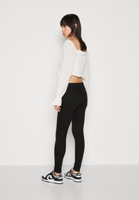 Hvit teksturert kort topp med lange ermer, kombinert med svarte slim-fit jeans og svarte-og-hvite joggesko. Settes fra baksiden.