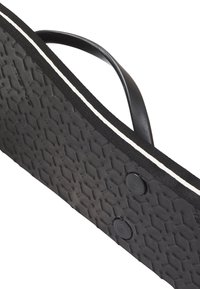 Svart flip-flop med texturerad gummi sula, vit accent längs kanten och ett flexibelt svart band. Har två cirkulära knappar på sulan.