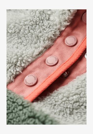 Pluizige groene en grijze stof met een gestructureerd oppervlak, met roze knopen en een koraalkleurige rand op een contrasterende perzikkleurige stoffen achtergrond.